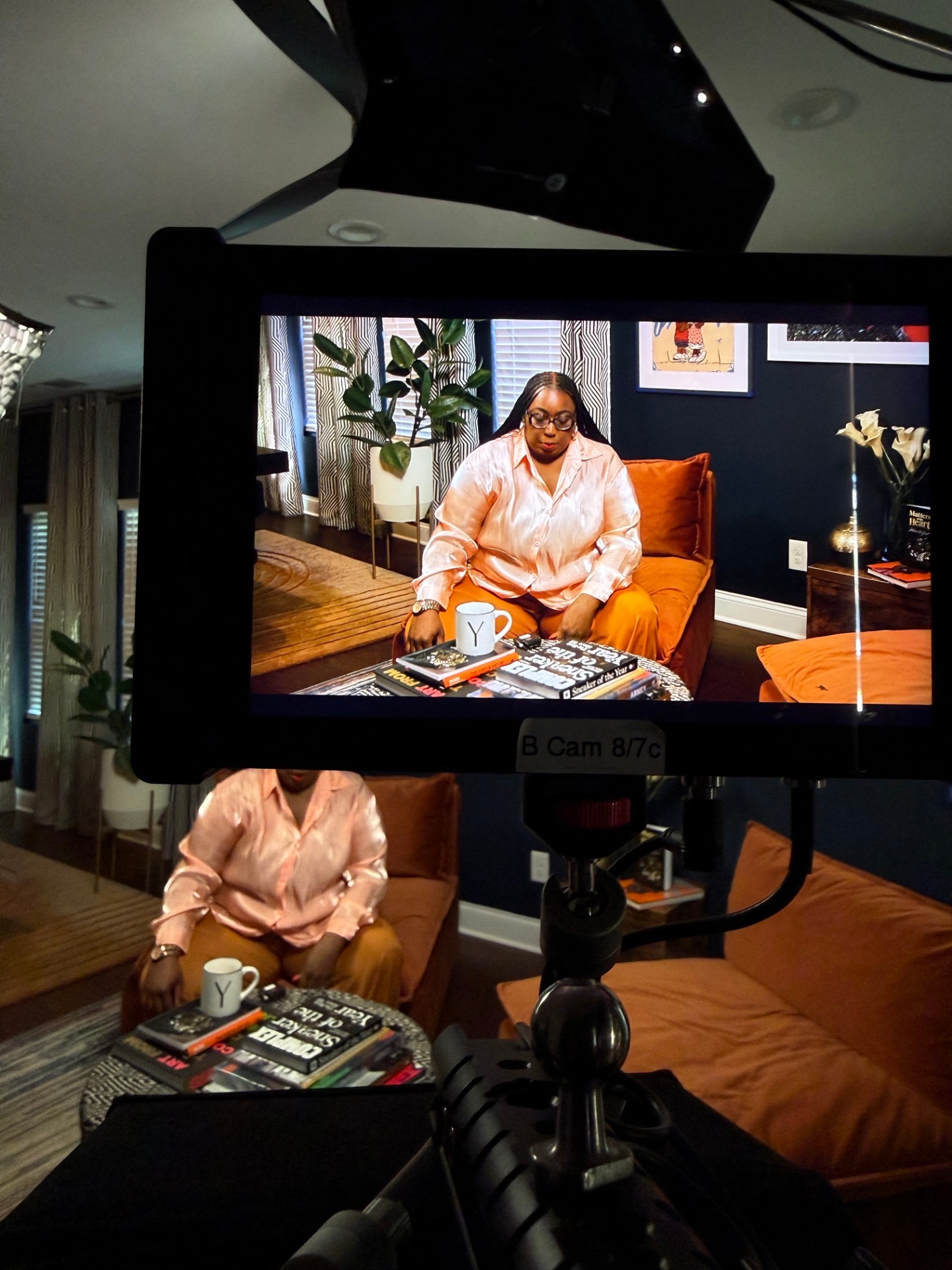 Monitor view of Madam Prezident in peach silk seated with sneaker culture books