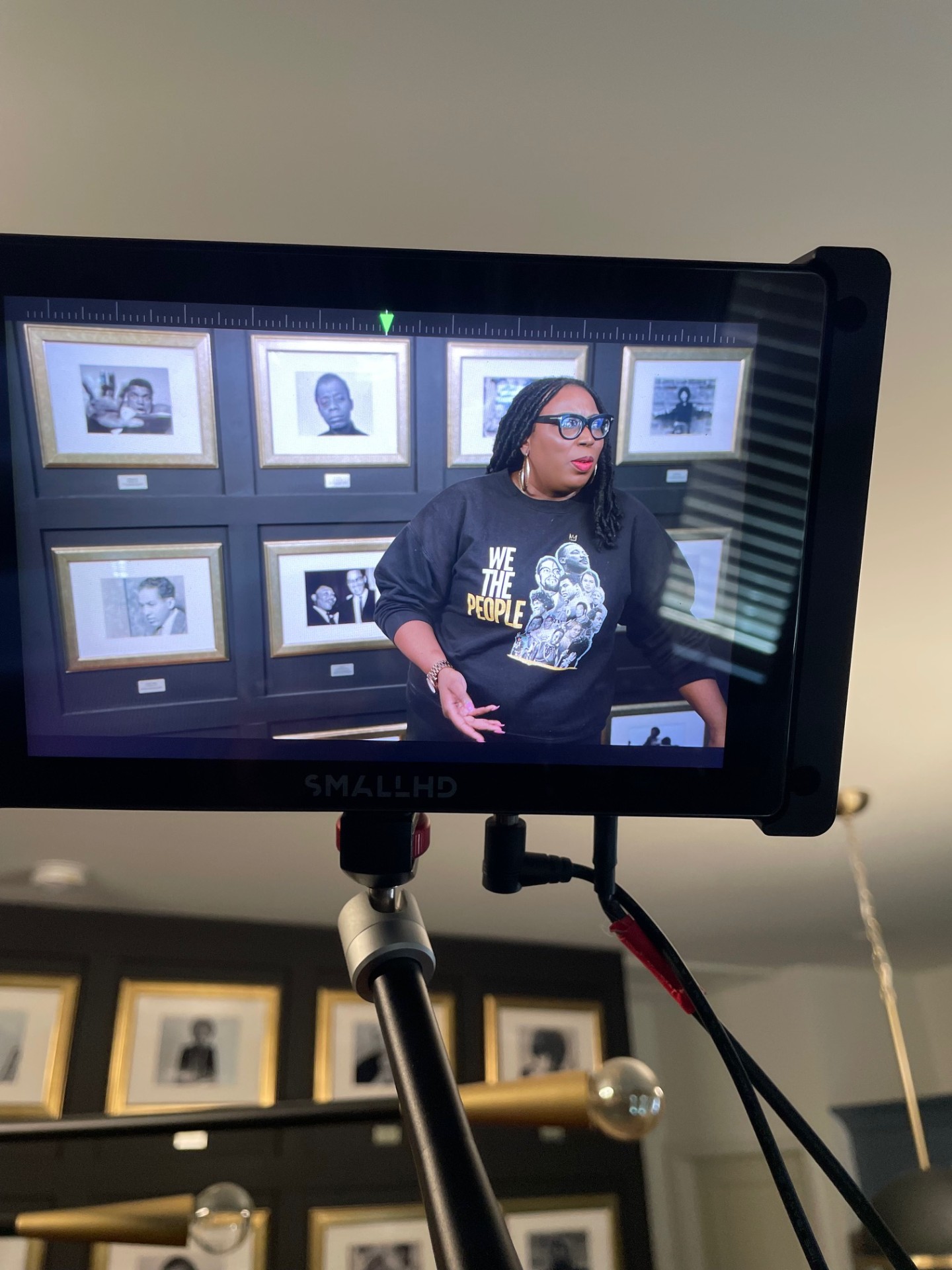 Madam Prezident in 'We The People' sweatshirt before wall of Black icon portraits