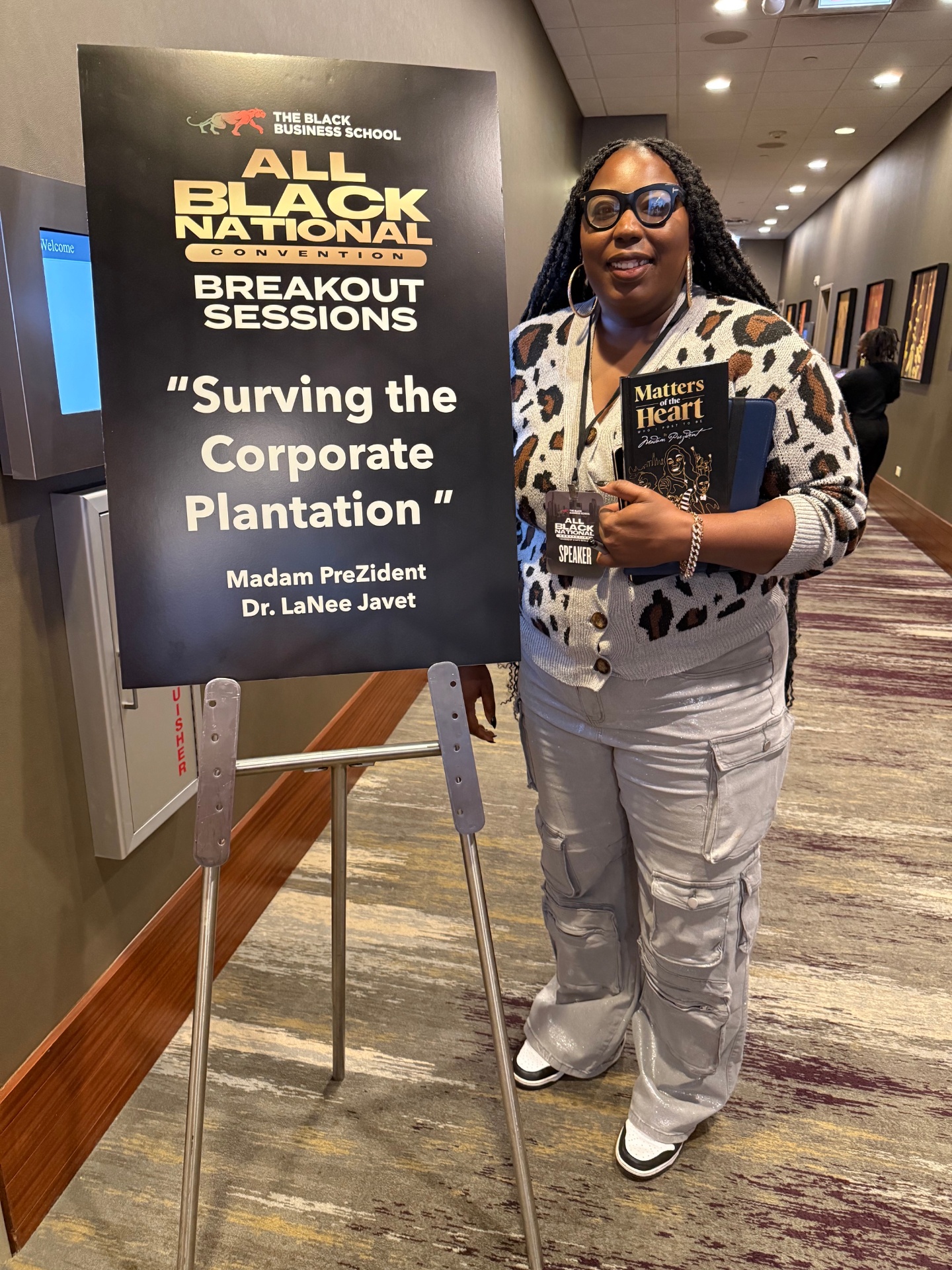 Madam Prezident next to All Black National Convention signage: Surviving the Corporate Plantation